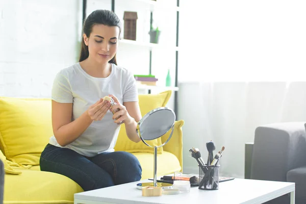 Portrait of young attractive woman doing makeup on sofa at home — Stock Photo