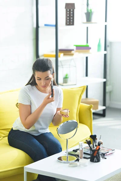 Retrato de mulher atraente aplicando blush rosto enquanto fazendo maquiagem em casa — Fotografia de Stock