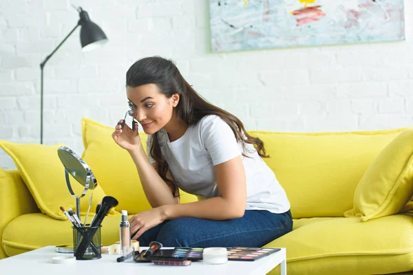 Side view of young woman looking at mirror while curling eyelashes with eyelash curler at home — Stock Photo