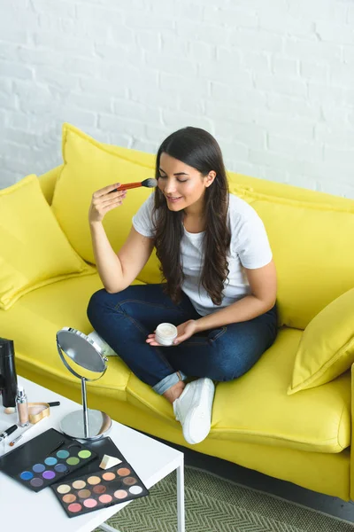 Vista ad alto angolo di donna sorridente con capelli lunghi che applica polvere mentre si siede sul divano a casa — Foto stock