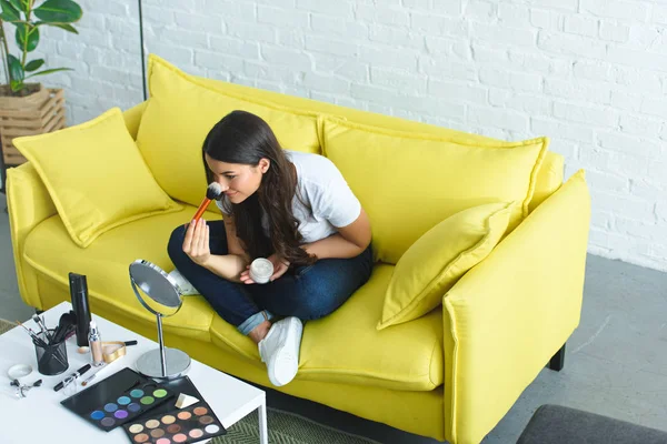 High angle view of beautiful woman with long hair applying powder while sitting on sofa at home — Stock Photo