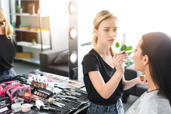 Selective focus of beautiful young woman getting makeup done by makeup artist — Stock Photo