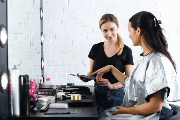 Jeune femme pointant vers la couleur sur la palette de maquillage dans les mains des maquilleurs — Photo de stock