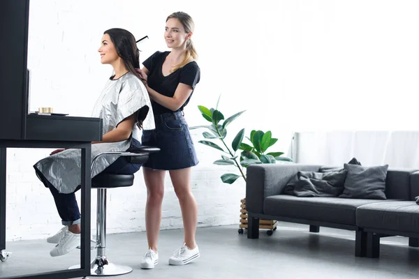 Side view of hairstylist with comb doing hairstyle for young smiling woman — Stock Photo