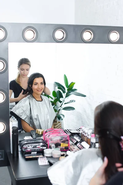 Mirror reflection of hairstylist doing hairstyle for young woman — Stock Photo