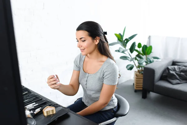 Side view of smiling woman taking selfie on smartphone while sitting at tabletop with cosmetics — Stock Photo