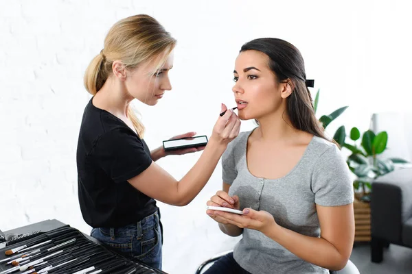 Atractiva mujer con teléfono inteligente conseguir maquillaje hecho por el artista de maquillaje - foto de stock