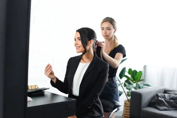 Focused hairstylist doing hairstyle while smiling businesswoman in suit taking selfie in mirror — Stock Photo