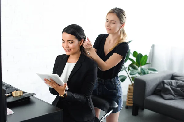 Cabeleireiro fazendo penteado enquanto sorrindo empresária de terno usando tablet digital — Fotografia de Stock