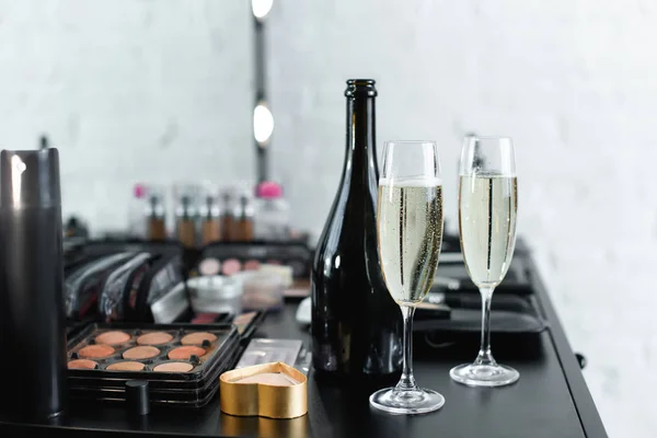 Close up view of bottle and glasses of champagne on tabletop with cosmetics for makeup — Stock Photo