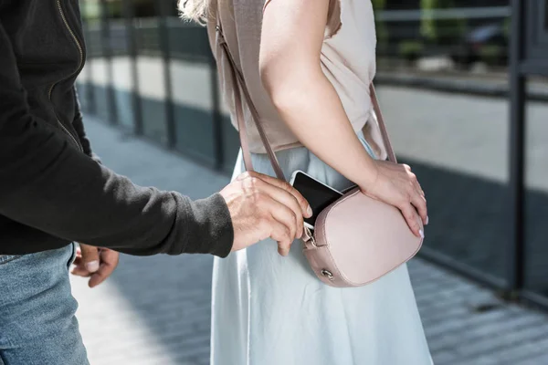 Vista recortada del hombre criminal carterista smartphone de la bolsa de las mujeres en la calle - foto de stock