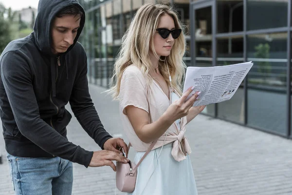 Woman reading newspaper while robber pickpocketing smartphone from her bag — Stock Photo