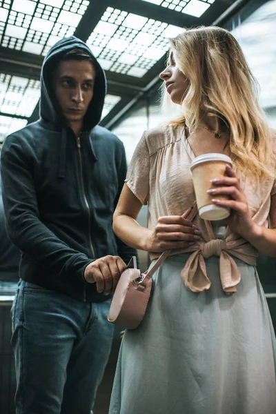 Male robbery pickpocketing smartphone from bag of woman with coffee in elevator — Stock Photo