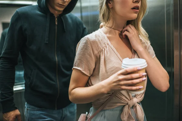 Cropped view of aggressive robber stealing pendant from womans neck in elevator — Stock Photo