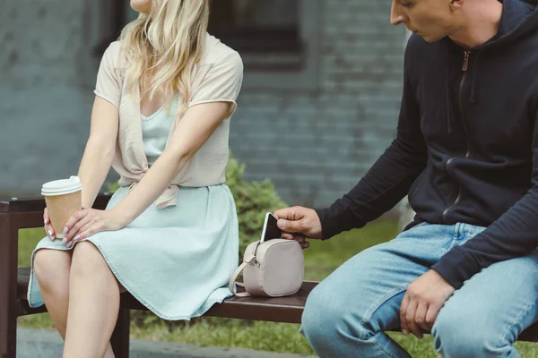 Robo pickpocketing smartphone de la bolsa de las mujeres en el banco en el parque - foto de stock