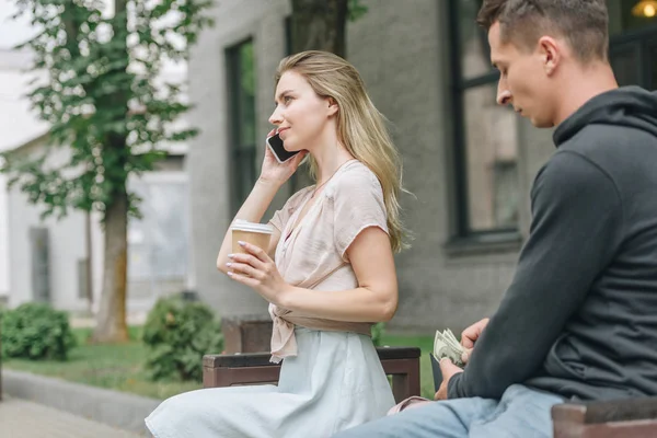 Homme pickpocketing argent de portefeuille tandis que la femme parle sur smartphone et boire du café dans le parc — Photo de stock