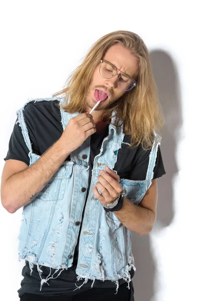 Young man in denim vest licking rolled joint on white — Stock Photo