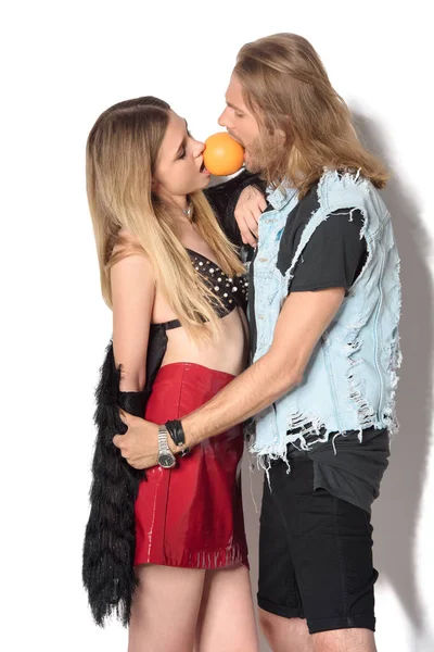 Stylish young couple embracing and biting orange from two sides on white — Stock Photo