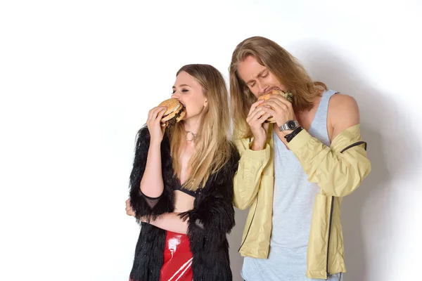 Hungry young couple eating tasty burgers on white — Stock Photo