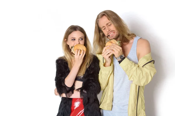 Hungry stylish young couple eating tasty burgers on white — Stock Photo
