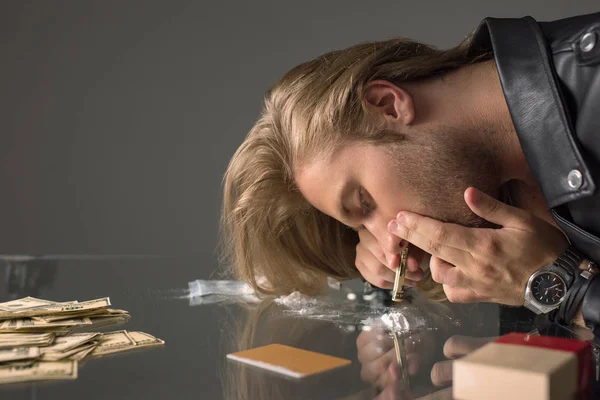 Vue latérale d'un jeune homme accro reniflant de la cocaïne depuis une table en verre — Photo de stock