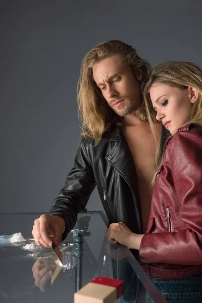 Young addicted couple with cocaine spilled on glass table on grey — Stock Photo