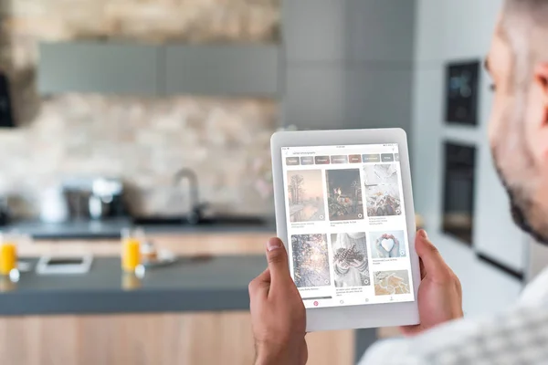 Selective focus of man using digital tablet with pinterest website on screen in kitchen — Stock Photo