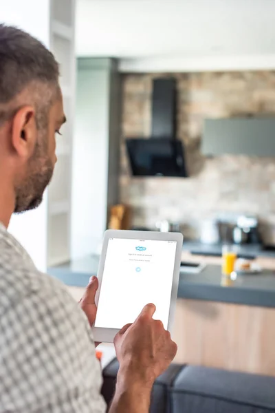 Selective focus of man using digital tablet with skype logo on screen in kitchen — Stock Photo