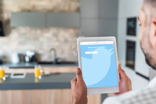 Selective focus of man using digital tablet with twitter logo on screen in kitchen — Stock Photo