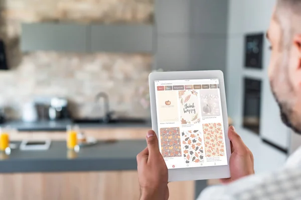 Selective focus of man using digital tablet with pinterest website on screen in kitchen — Stock Photo