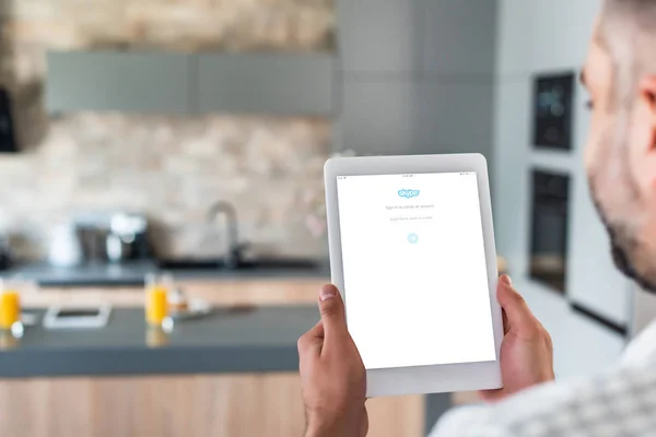 Enfoque selectivo del hombre utilizando tableta digital con logotipo de skype en la pantalla en la cocina - foto de stock