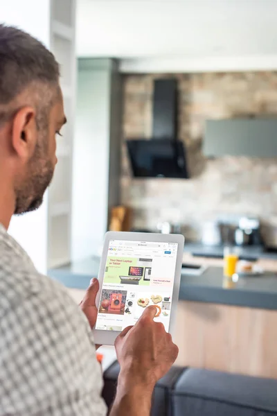 Selective focus of man using digital tablet with ebay website on screen in kitchen — Stock Photo