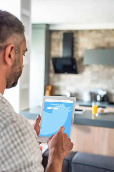 Enfoque selectivo del hombre utilizando tableta digital con el logotipo de twitter en la pantalla en la cocina - foto de stock