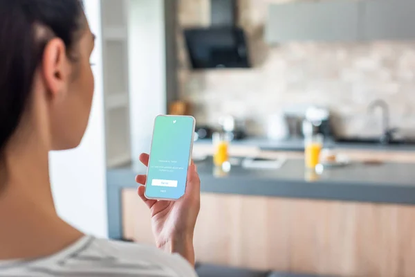 Selective focus of woman holding smartphone with twitter logo on screen in kitchen — Stock Photo