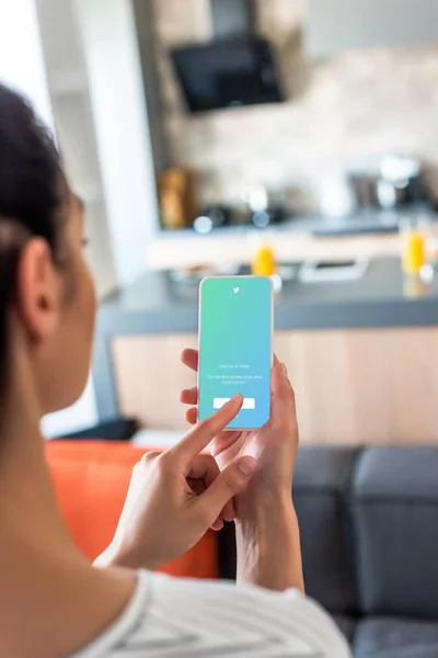 Selective focus of woman using smartphone with twitter logo on screen in kitchen — Stock Photo