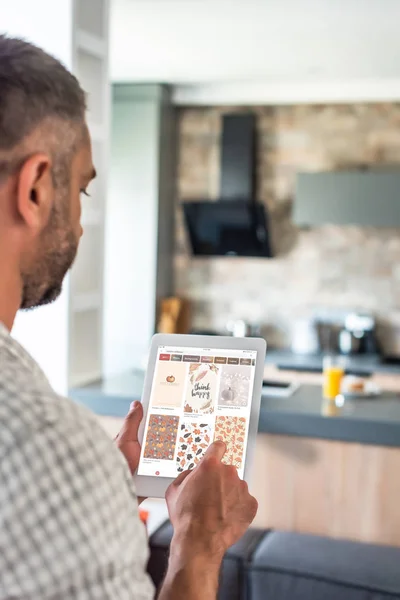 Selective focus of man using digital tablet with pinterest website on screen in kitchen — Stock Photo