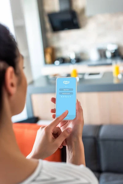 Enfoque selectivo de la mujer utilizando el teléfono inteligente con logotipo de Skype en la cocina - foto de stock