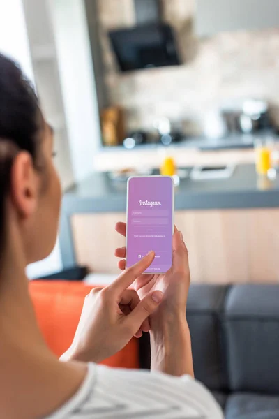 Enfoque selectivo de la mujer utilizando el teléfono inteligente con el logotipo de instagram en la cocina - foto de stock