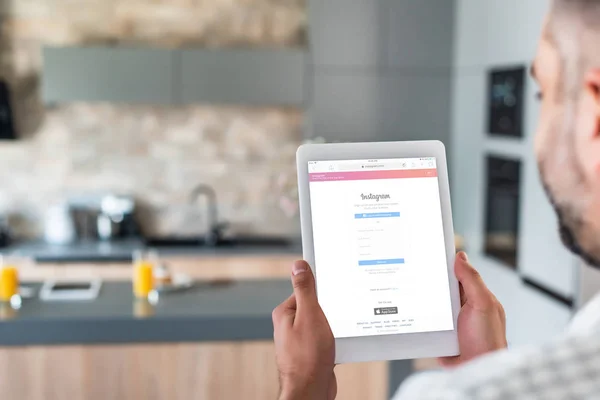 Selective focus of man using digital tablet with instagram logo on screen in kitchen — Stock Photo