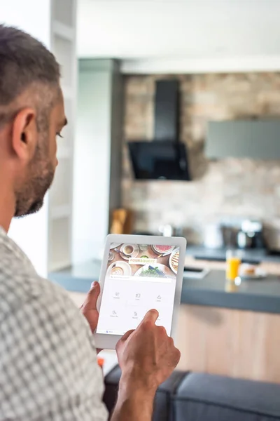 Selective focus of man using digital tablet with foursquare website on screen in kitchen — Stock Photo