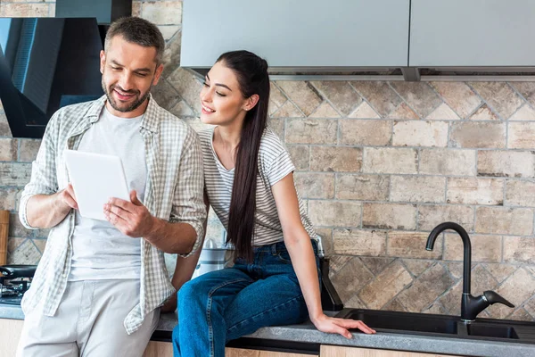 Retrato de pareja sonriente usando tableta digital juntos en la cocina, concepto de hogar inteligente - foto de stock