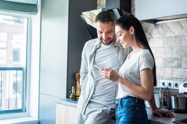 Coppia sorridente utilizzando smartphone insieme in cucina, concetto di casa intelligente — Foto stock