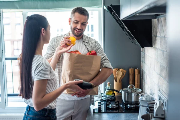 Couple marié avec paquet de papier plein de légumes frais pour le dîner dans la cuisine à la maison — Photo de stock