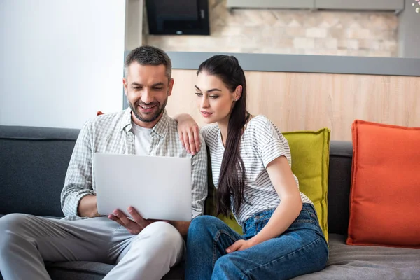 Porträt eines Paares, das gemeinsam Laptop benutzt, während es sich zu Hause auf dem Sofa ausruht — Stockfoto