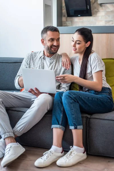 Casal usando laptop juntos enquanto descansa no sofá em casa — Fotografia de Stock