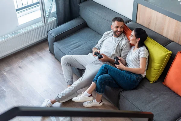 Visão de alto ângulo do casal com gamepads olhando um para o outro enquanto joga jogos de vídeo juntos em casa — Fotografia de Stock