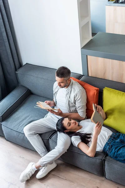 Vue grand angle des livres de lecture de couple sur le canapé à la maison — Photo de stock