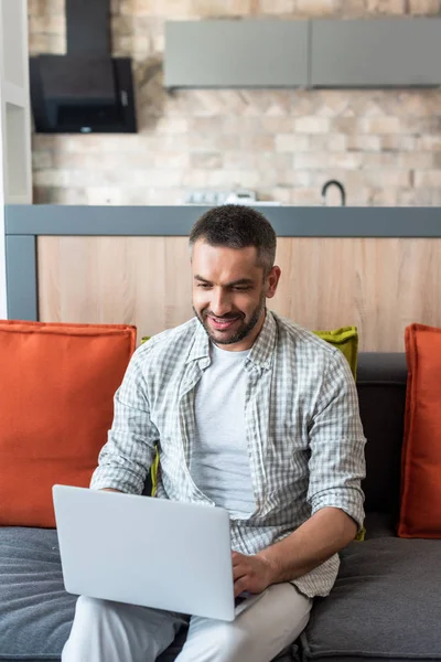 Portrait of smiling man using laptop on couch at home — Stock Photo