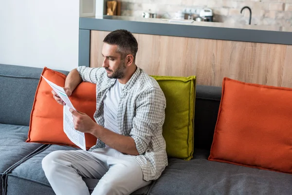 Retrato de homem focado lendo jornal no sofá em casa — Fotografia de Stock