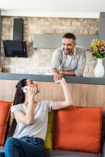 Wife talking on smartphone and holding hands together with husband at home — Stock Photo